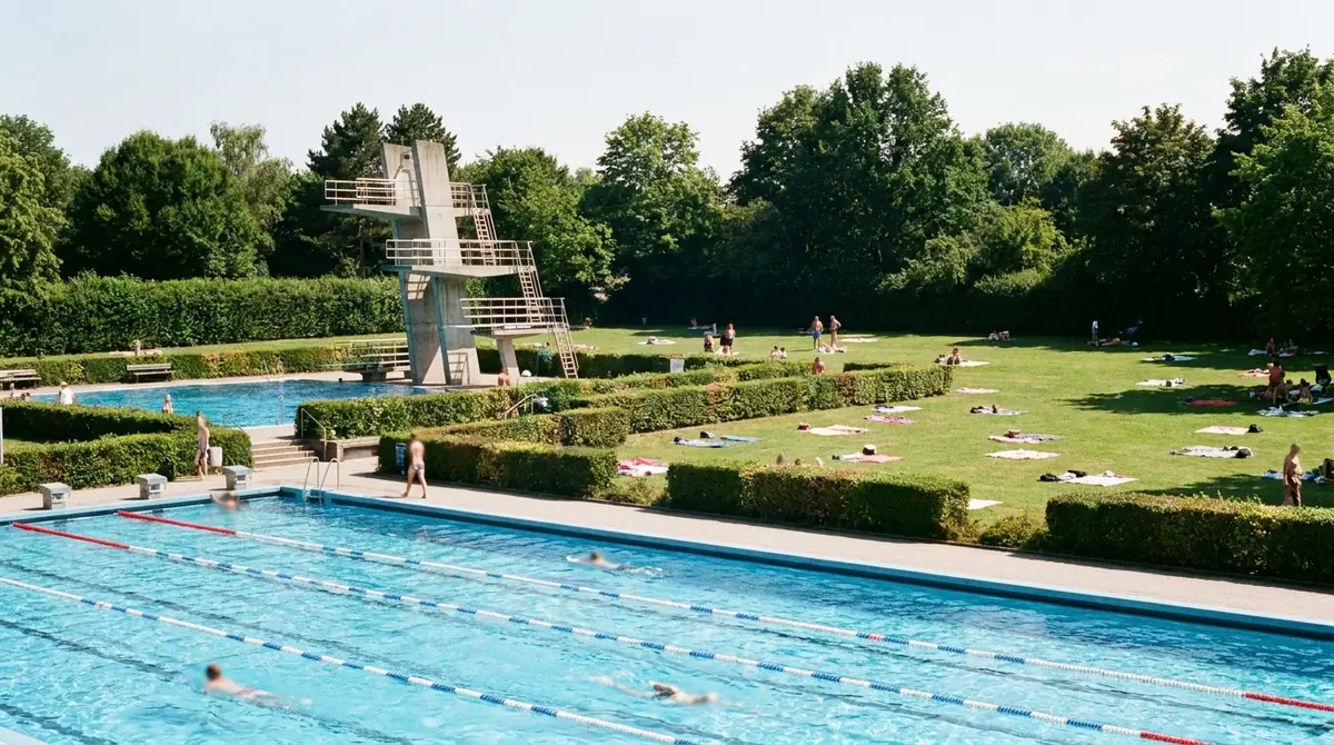 Freibad mit 50-Meter-Sportbecken, Bahnleinen, Sprungturm und Liegewiese im Sommer